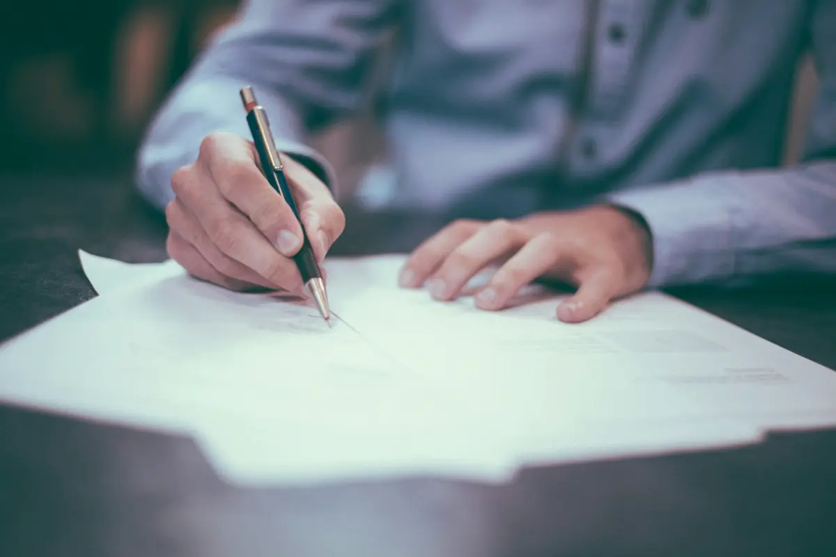 Persona firmando un contrato en una mesa de oficina, parte del cumplimiento normativo de las aseguradoras